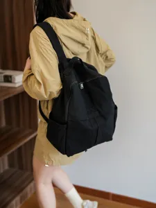 Vue détaillée d'un sac à dos noir minimaliste en toile porté dans un intérieur confortable.