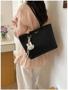 Detail shot of a black minimalist large capacity tote shoulder bag with cute rabbit pendant.