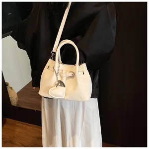 Chic white woven bucket bag for women, stylish crossbody handbag with heart charm and handle.