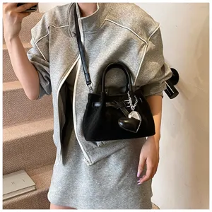 Black woven leather shoulder bag detail with metal heart charm and chic casual outfit.