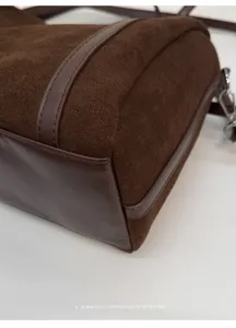 Primer plano detallado de la textura y costuras del bolso de hombro de ante y cuero marrón.