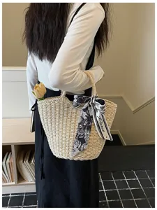 Primo piano sui dettagli della borsa in paglia intrecciata con elegante foulard in bianco e nero.