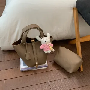 Detail view of chic bucket bag with matching pouch and cute plush charm on wooden floor.
