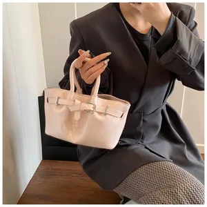 Detail shot of pink patent leather handbag featuring elegant front strap buckle design and dual top handles.