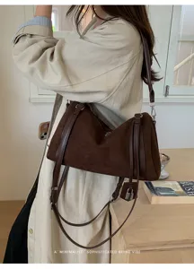 Vista detallada de un bolso de hombro de ante marrón con correas oscuras puestas.