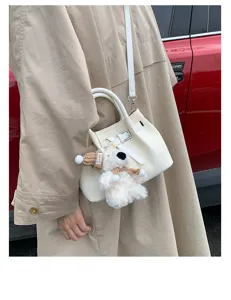 Detailed view of white pleated bucket handbag featuring cute plush bear keychain and long strap.