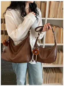 Close-up detail view of stylish brown leather hobo shoulder bag with plush charm in scene.