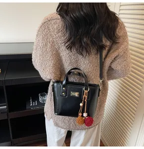 Detailed back view of a black glossy bucket bag with pom-pom charms, shown worn indoors.