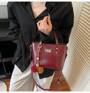 Detail shot of a stylish wine red leather bucket bag with metal charm, women crossbody.
