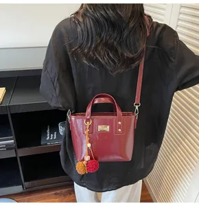 Detail view of stylish burgundy women handbag with cute pom pom charm and shoulder strap.
