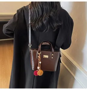 Detail view of brown leather bucket bag with metal plaque and cute pom-pom charms.