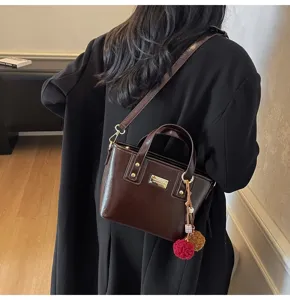 Detail view of stylish dark brown patent leather handbag with pom-pom charm and metal plaque.