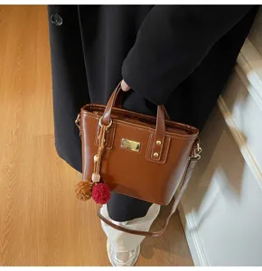Detailed view of the stylish brown leather bucket bag with cute pom-pom charm and handles.