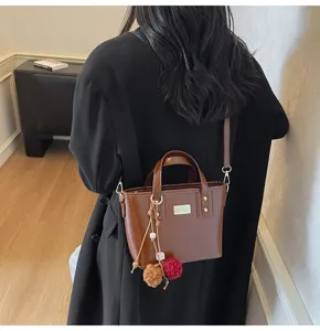 Detailed view of the brown PU bucket bag with cute pendants and elegant metal logo accent.