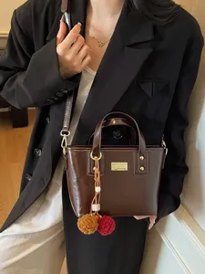 Stylish brown patent leather bucket bag with cute pom-pom charms for women autumn winter fashion.