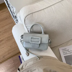 Grey womens mini top handle crossbody bag with large buckle detail on white textured sofa
