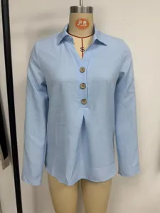 Primo piano della camicia azzurra a maniche lunghe con colletto chic e grandi bottoni in legno.