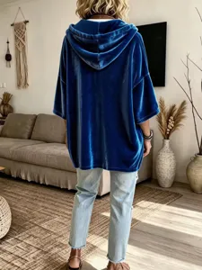 Detail view of blue velvet hoodie back, showing soft texture and loose fit style in home setting.