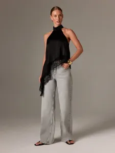 Schwarzes Satintop mit Halfter und zarter Spitzenborte, elegant kombiniert mit grauen Jeans.