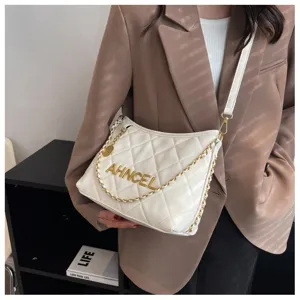 Detail view of stylish white quilted shoulder bag with gold chain strap and metallic letters.