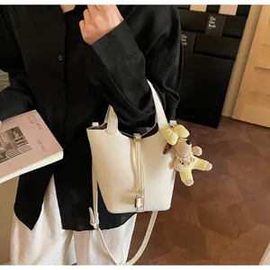 Stylish white leather bucket bag with cute dog pendant, versatile commuter shoulder bag.