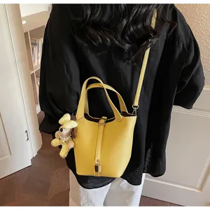 Detail view of stylish yellow leather bucket bag with top handles, lock charm, and cute bear pendant.