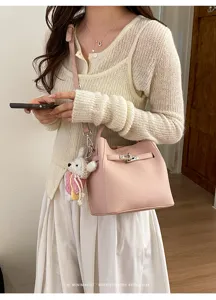 Detailansicht der rosa Flecht-Leder-Eimer Tasche mit Metallschloss und süßem Anhänger.
