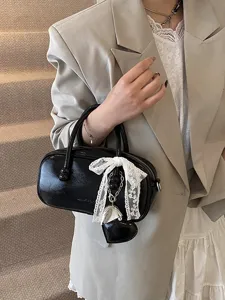 Stylish black patent leather bowling bag with cute lace bow pendant, versatile chic handbag.
