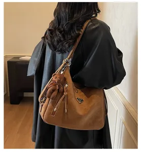Detailed view of retro brown shoulder bag featuring chic metal triangle logo and cute bear pendant.