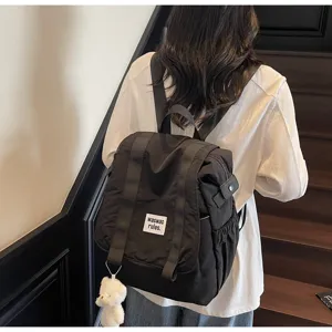 Detail view of the casual black nylon backpack featuring a white patch and cute bear pendant.