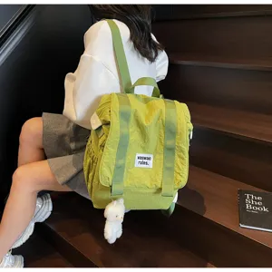 Casual green nylon backpack detail shot, lightweight travel school bag with cute bear pendant.