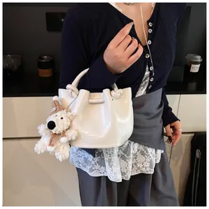 Stylish white PU leather bucket bag with cute bear pendant, trendy knotted handle design.