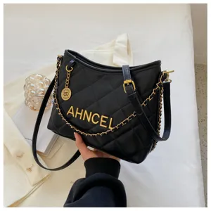 Detail view of black quilted bucket bag with gold chain strap and metal lettering detail.