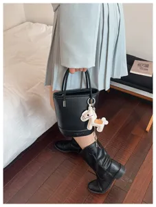 Detailed view of black litchi pattern leather bucket handbag with cute horse charm accessory.