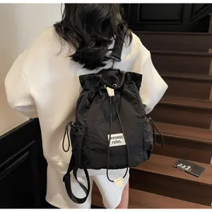 Detail view of casual black canvas drawstring backpack on model, showing side pocket design.