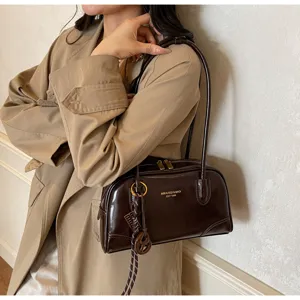 Detailed view of the retro brown patent leather shoulder pillow bag worn by model.