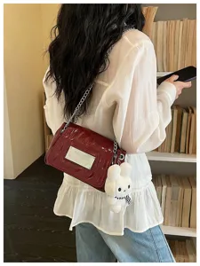Red patent leather shoulder bag detail, elegant chain strap and cute plush bunny keychain.