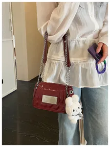 Detail shot of wine red patent leather chain crossbody bag with cute bunny plush charm for women.