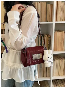 Chic dark red patent leather shoulder bag with chain strap and cute white bunny plush charm.