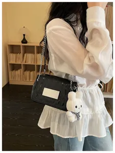 Detailed view of a black patent leather shoulder bag with chain strap and cute plush bunny.