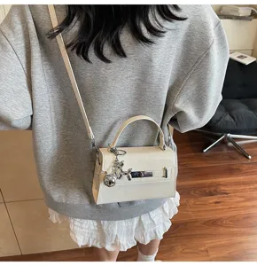 Detail shot of chic white leather crossbody bag featuring metal lock and cute balloon dog charm.