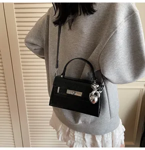 Black textured top handle bag, elegant crossbody style with metal lock and bear charm.