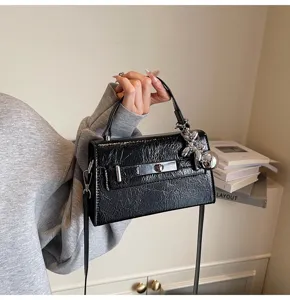 Black textured Kelly crossbody shoulder bag with metal turn lock and cute charm pendant.