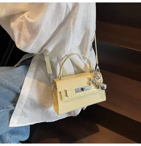 Detailed view of trendy yellow patent leather Kelly handbag featuring metal charm and lock.