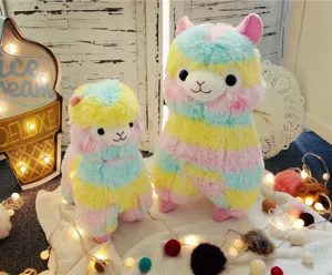 Close-up shot of colorful rainbow alpaca plush toys on a cozy warm fairy light blanket.