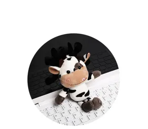 Close-up of a cute black and white cow plush toy pendant sitting on a keyboard.