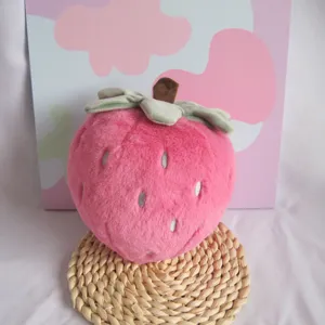 Close up of pink strawberry plush toy with green leaves, soft stuffed doll texture.