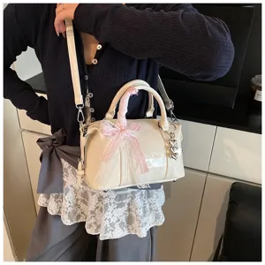 Detail shot of a chic cream pillow handbag featuring a pink bow ribbon and heart charm accent.