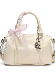 Cream patent leather shoulder bag with pink lace ribbon and heart pendant, chic pillow handbag.