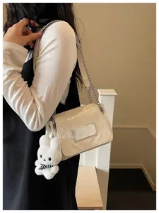Close-up detail of stylish women's shoulder bag with chain strap and cute plush bunny charm.